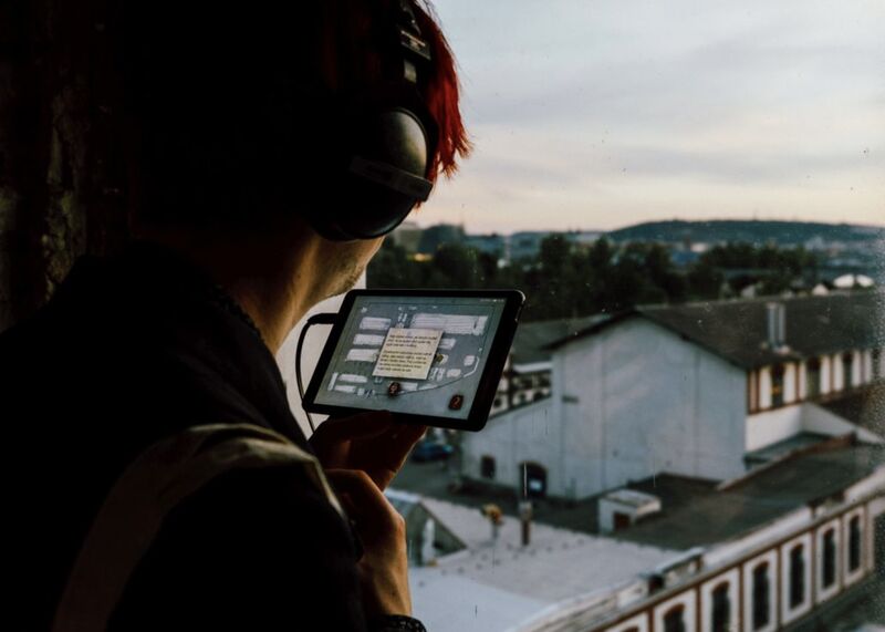 A visitor in Neviditelná Tržnice with headphones and the tablet app, by a window over the market halls